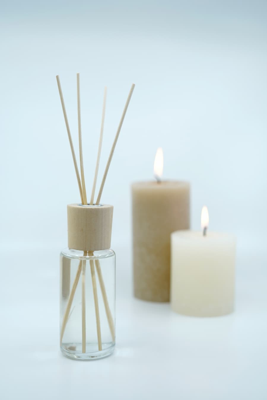 Two neutral candles positioned in the background with a reed diffuser in the foreground