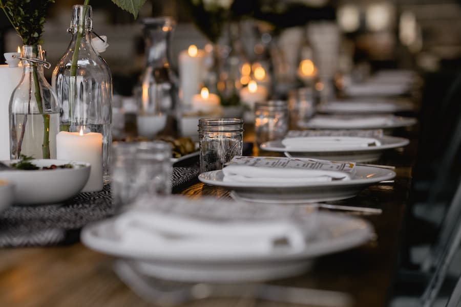 Tablescape setting with rows of white plates on a table decorated with glassware and candles
