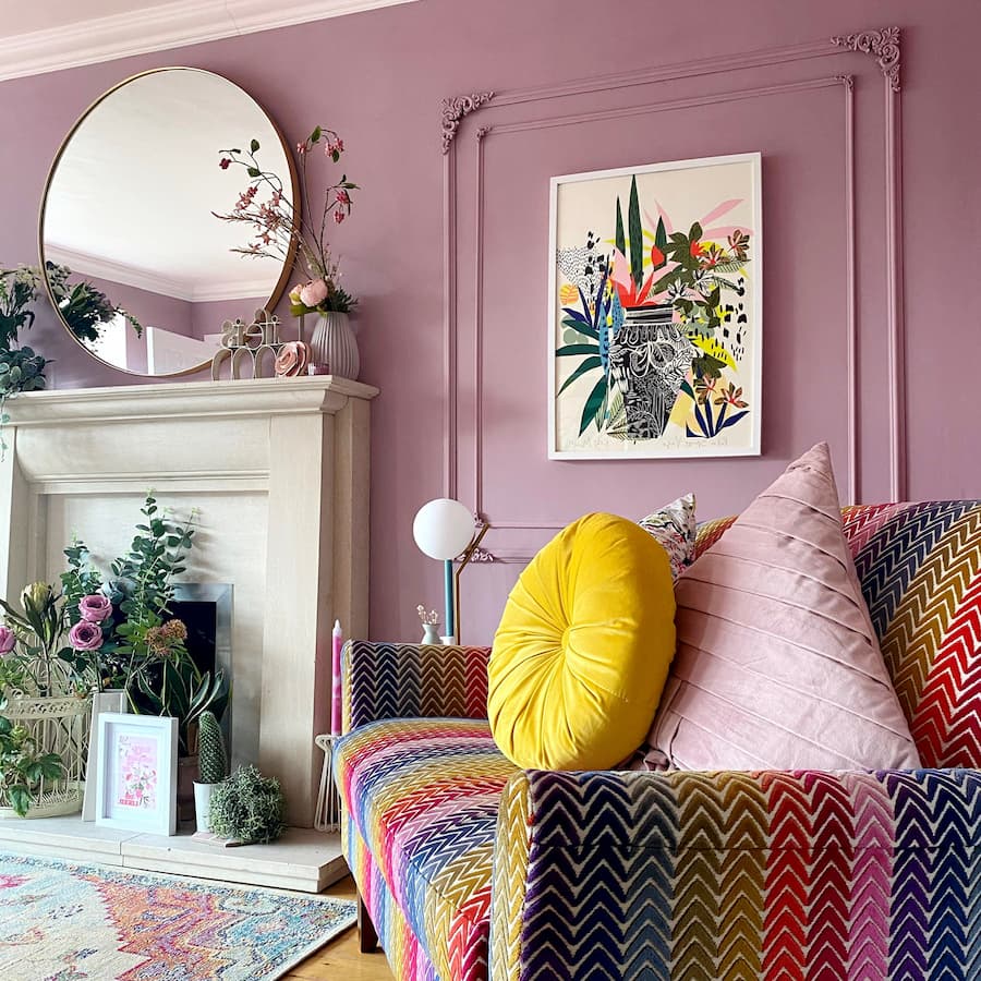 Pastel pink painted wall with panelled detail included to showcase a painting. There's a brightly coloured zig-zag chair in the foreground