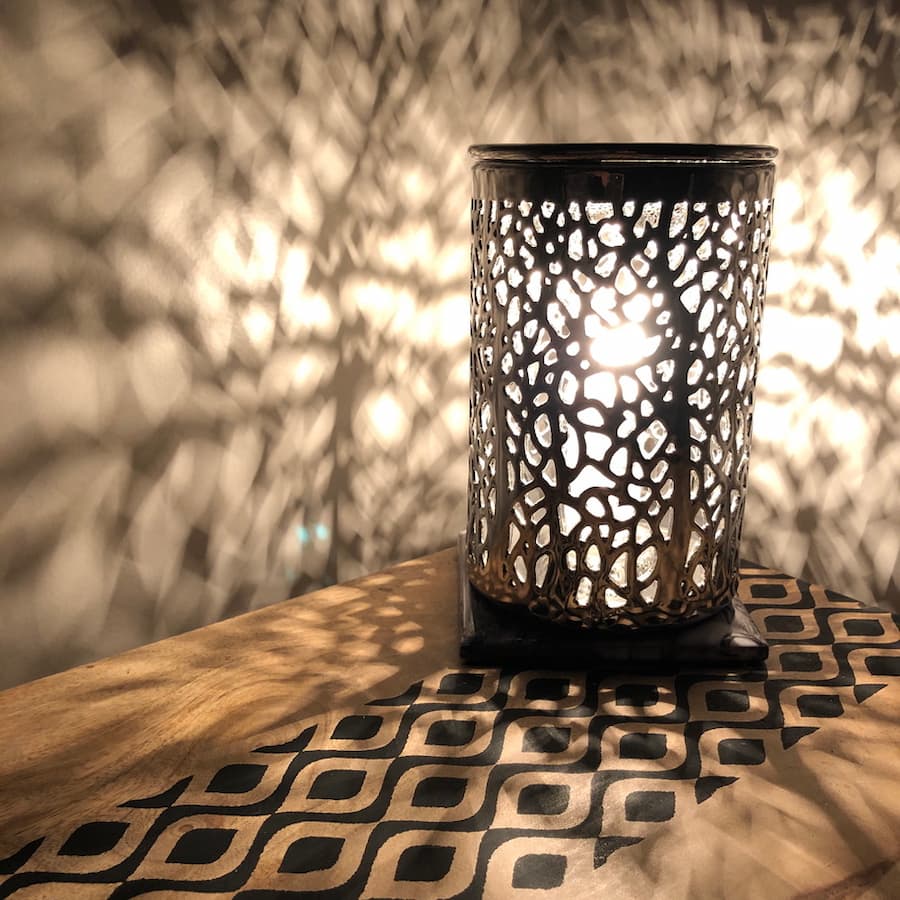 Decorative table lamp giving off a warm white glow. The pattern of the lamp is reflected on the wall.