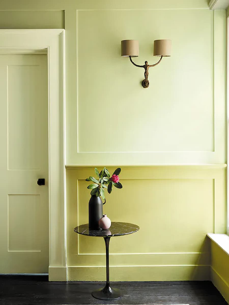 Wall painted in two different tones of a yellow/green tone using Little Greene paint. The top section of the wall is painted a lighter tone to the lower panelled section