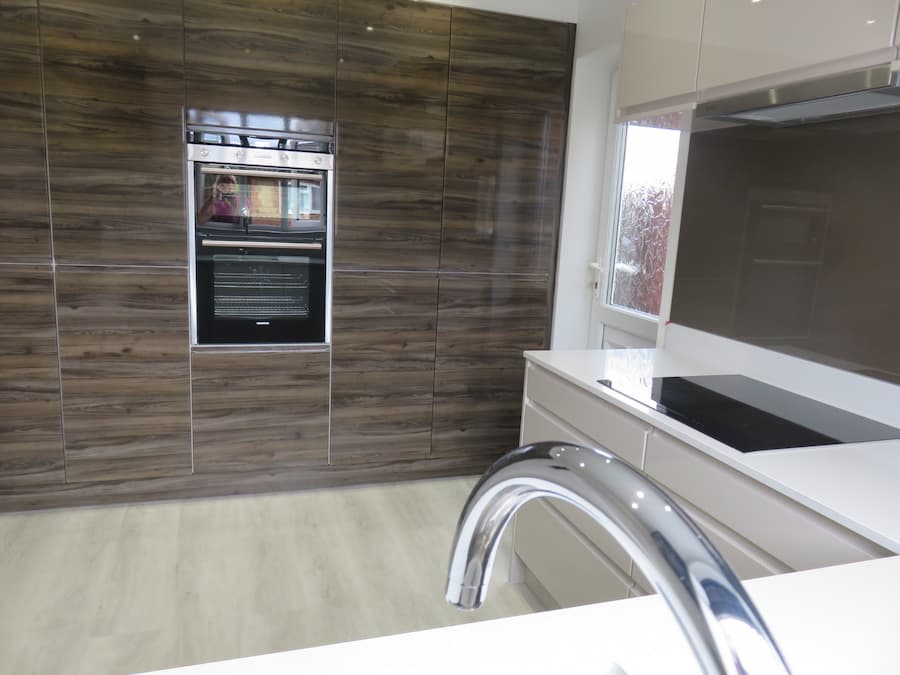 Modern kitchen design Back wall with floor to ceiling high gloss walnut cupboards and a double oven positioned in the centre