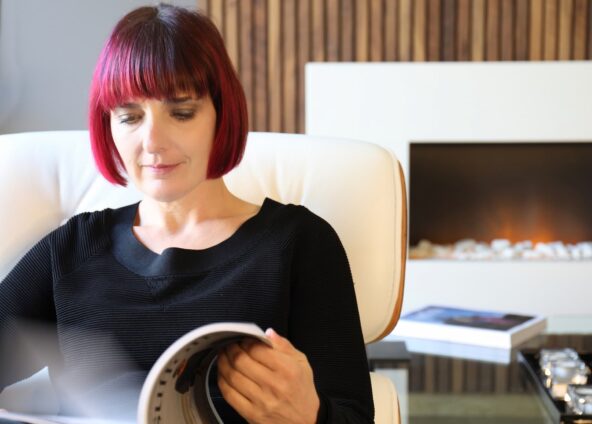 female with red hair sat in a white chair flicking through a magazine