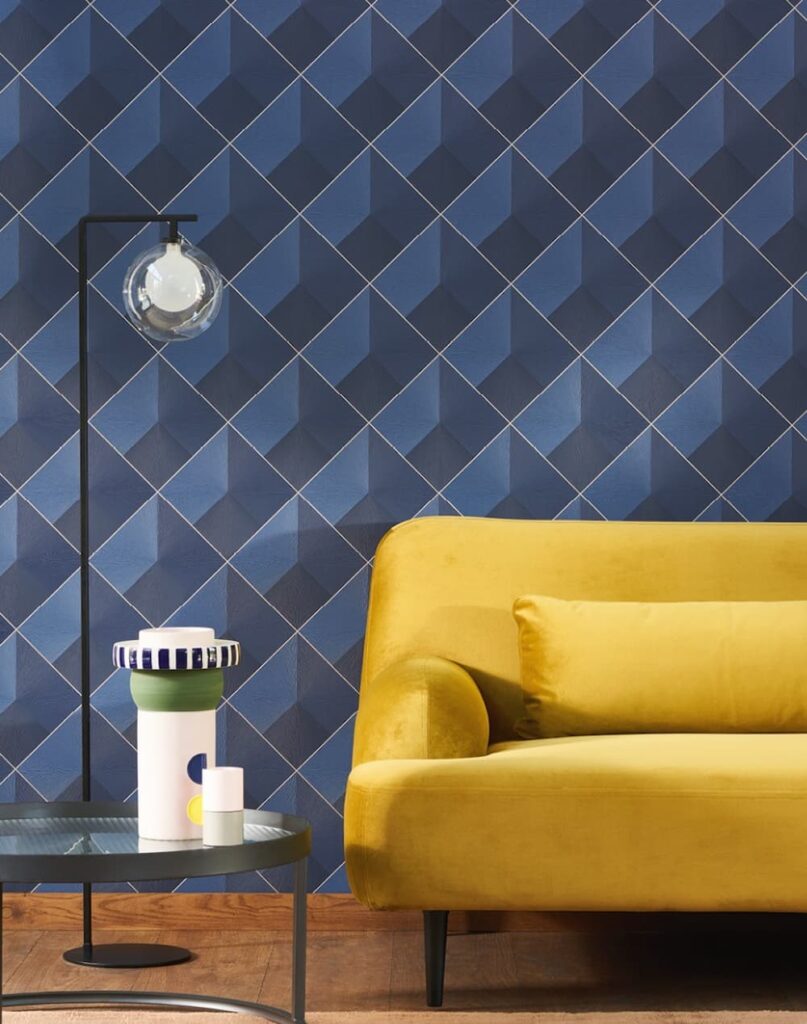 Bold geometric wallpaper design using two tones of blue and a bright yellow sofa in the front