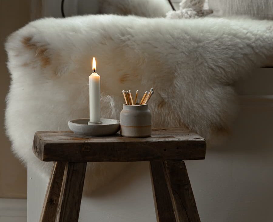 Off-white sheepskin rug in the background and ceramic candle holder and candles on a stool