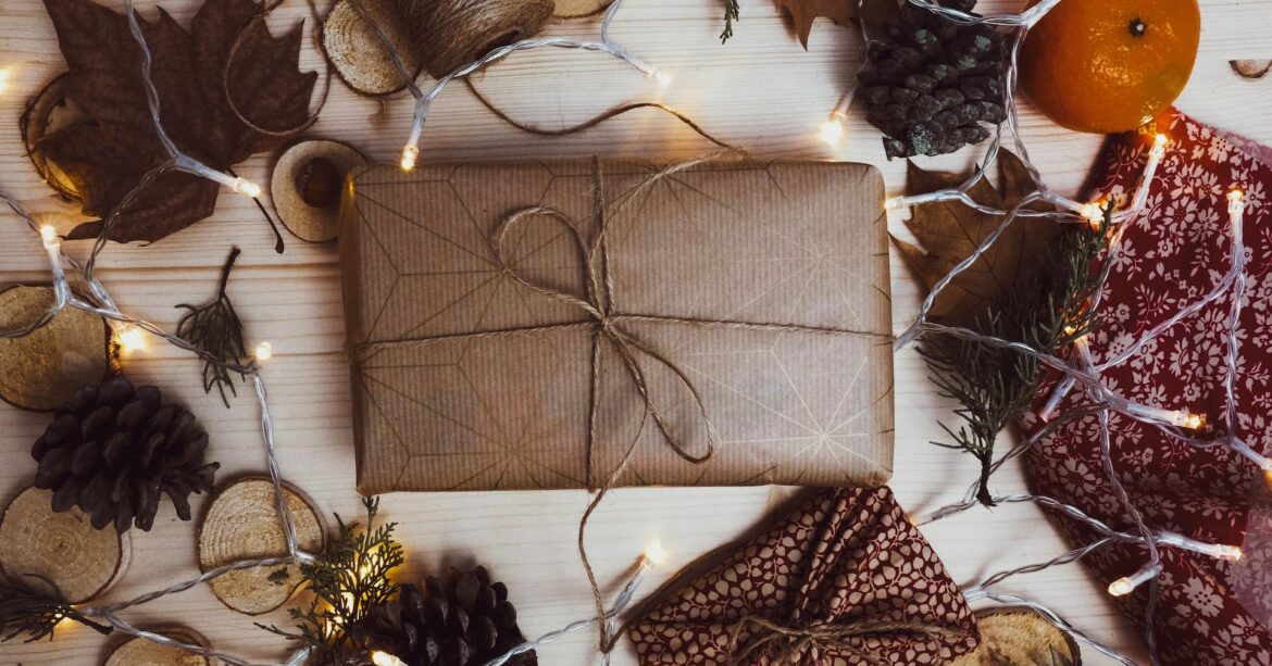 Flat lay of a gift wrapped in brown paper and autumnal accessories and Christmas lights placed around the edge