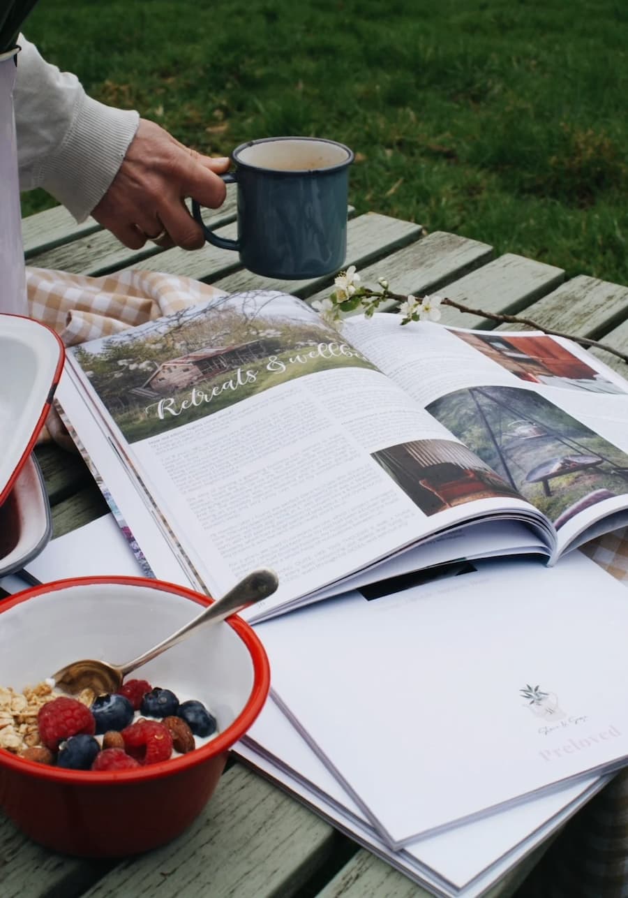 Preloved magazine opened on an outdoor table with someone putting a mug of tea down by the side of it