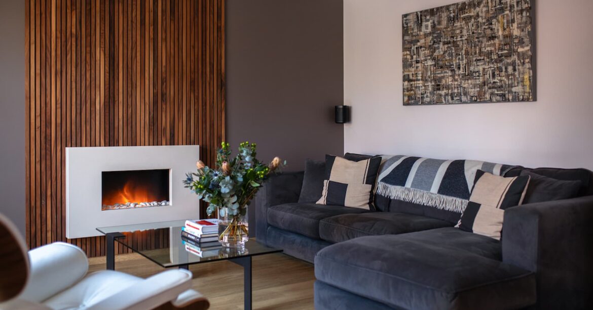 Interior design trends 2024 Modern living room with walnut feature wall and marble electric fire positioned in the centre with grey corner sofa and modern glass coffee table following one of the interior design trends for 2024